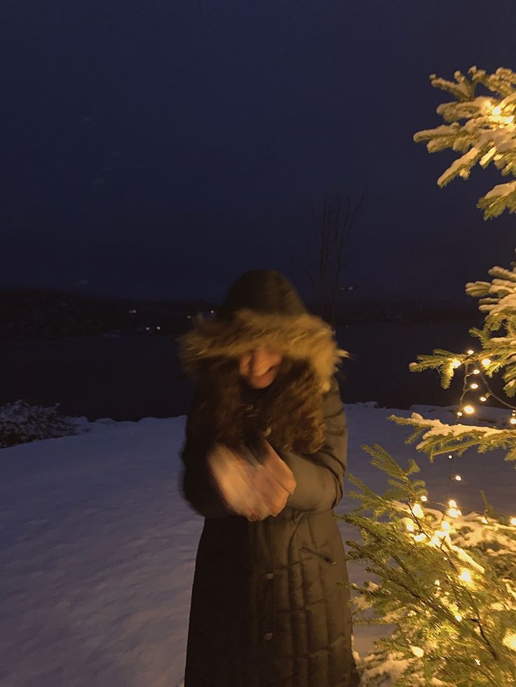 a woman standing in front of a christmas tree with lights on it's branches