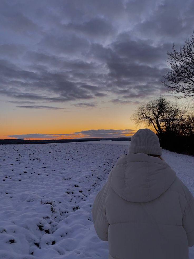 a person standing in the middle of a snow covered field at sunset or dawn,