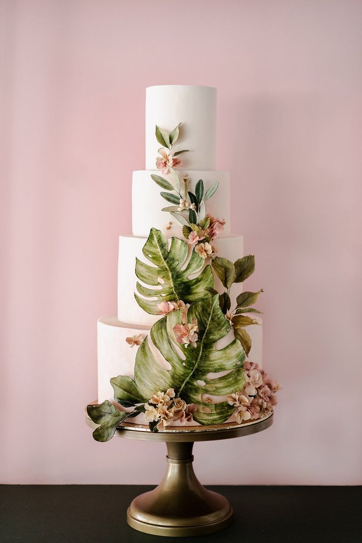 a three tiered wedding cake decorated with tropical leaves and flowers