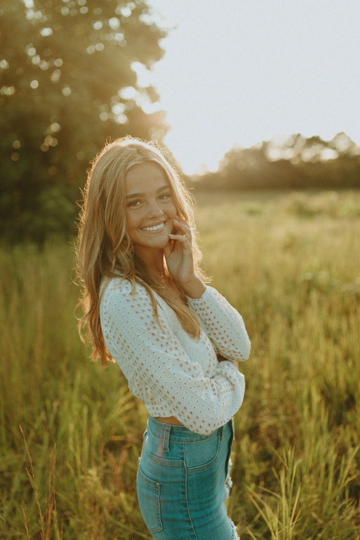 a woman standing in the middle of a field talking on a cell phone and smiling