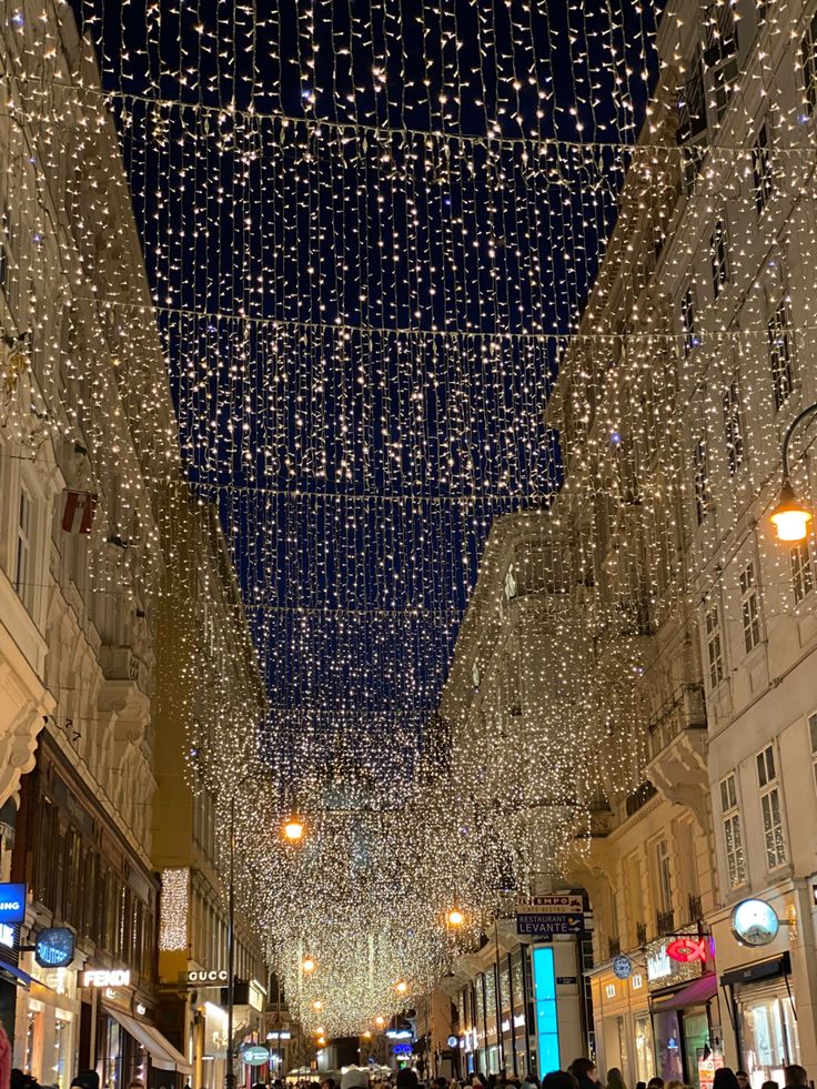 people are walking down the street with lights hanging from the ceiling and on the buildings