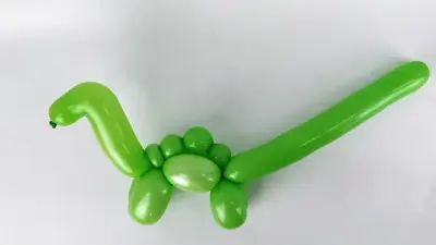 a green balloon shaped like a dinosaur with its tail curled up and eyes closed, sitting on a white surface