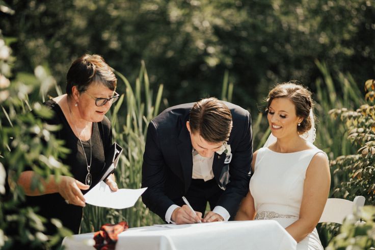 a bride and groom signing their marriage vows at the altar in front of some trees