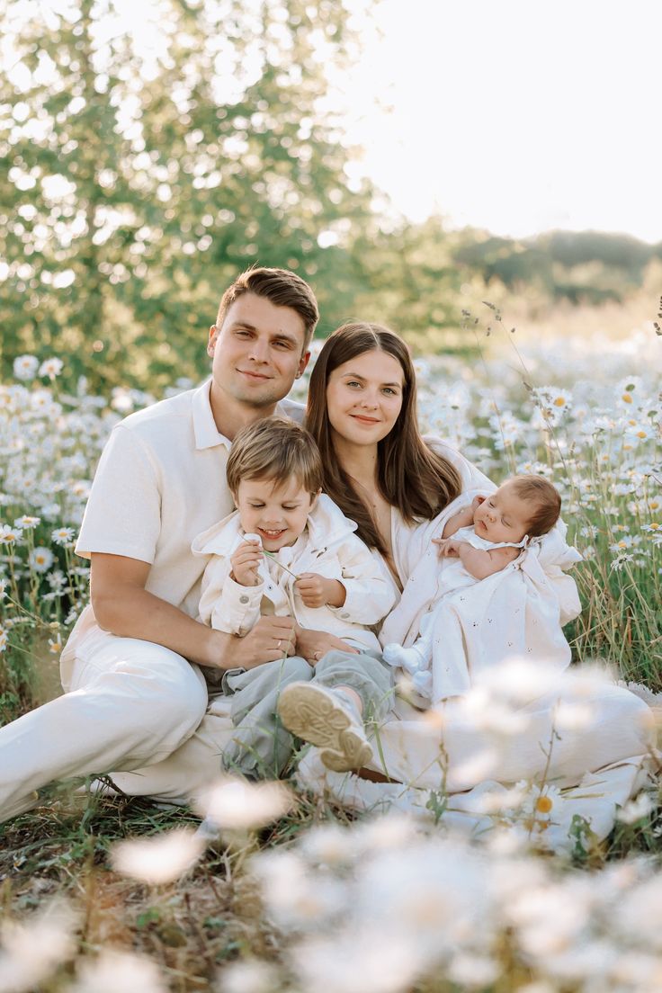 a family sitting in the middle of a field with daisies and trees behind them