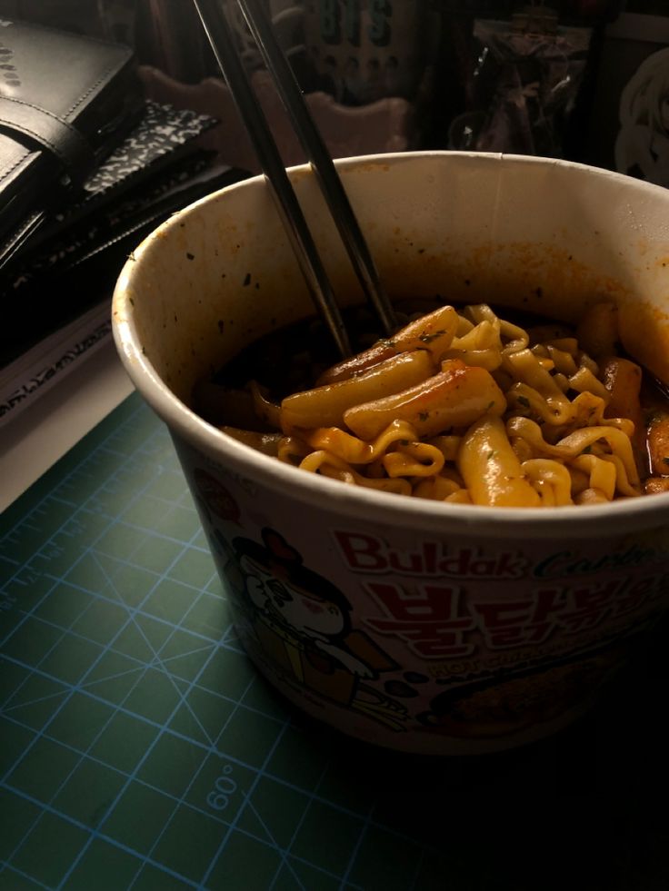 a bowl of noodles with chopsticks in it on a table next to a book