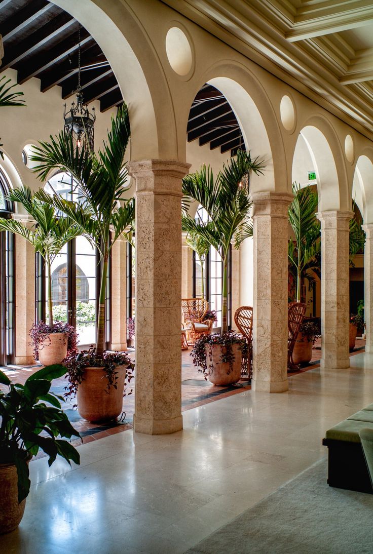 an indoor area with potted plants and benches in the center, surrounded by arches