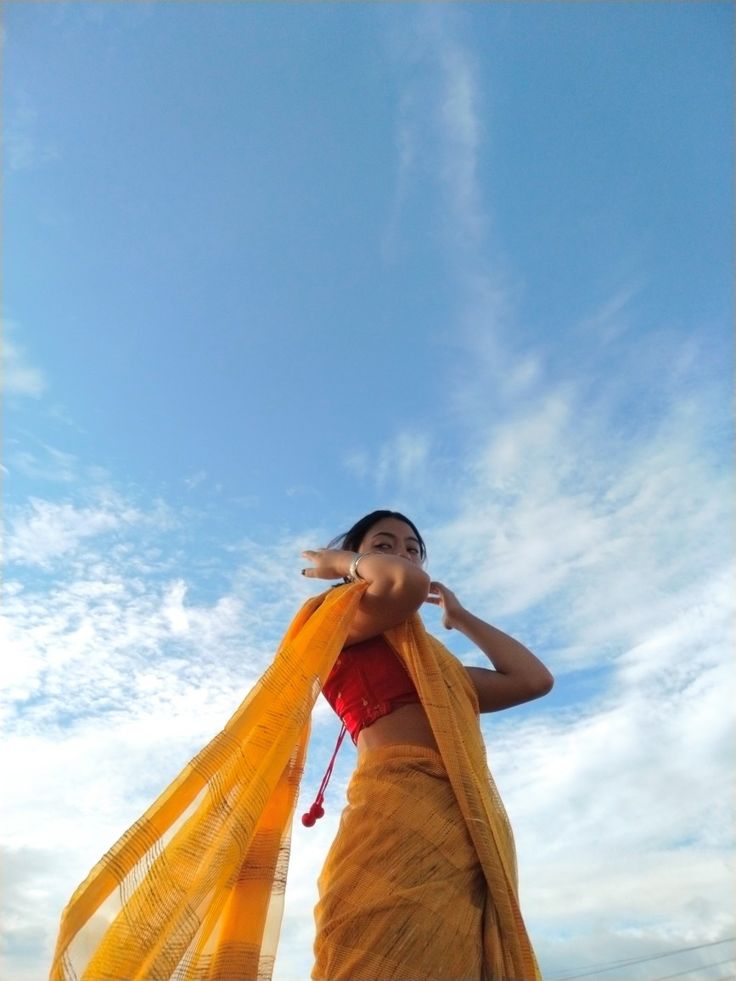 a woman wearing a yellow sari standing under a blue sky