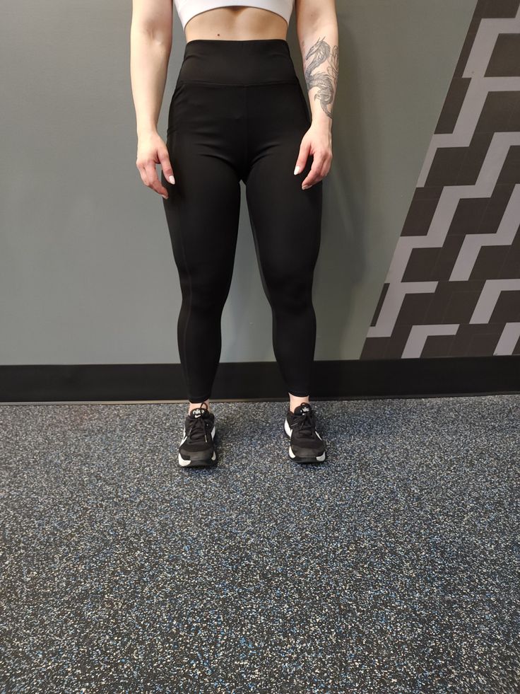 a woman standing in front of a wall wearing black leggings and a white crop top