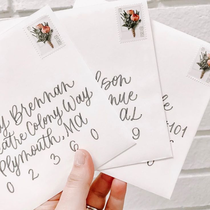 three envelopes with writing on them are being held up by someone's hand