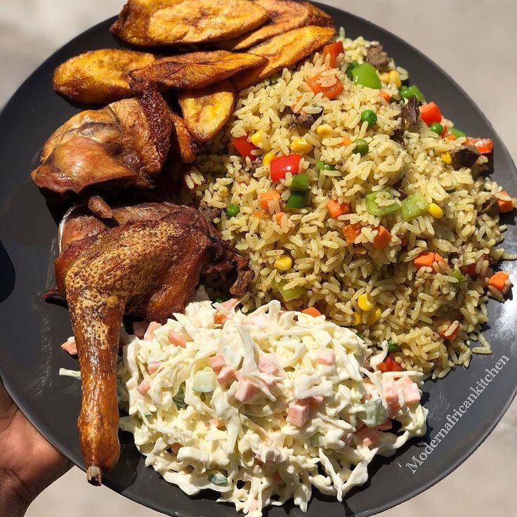 a plate with rice, meat and vegetables on it is being held by a person