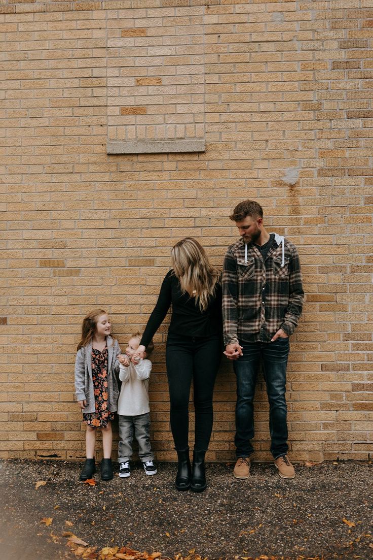 a family standing in front of a brick wall holding hands and looking at the camera