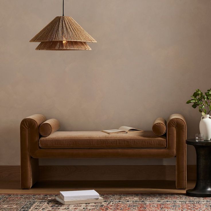 a brown couch sitting next to a table with a vase on it and a lamp hanging from the ceiling