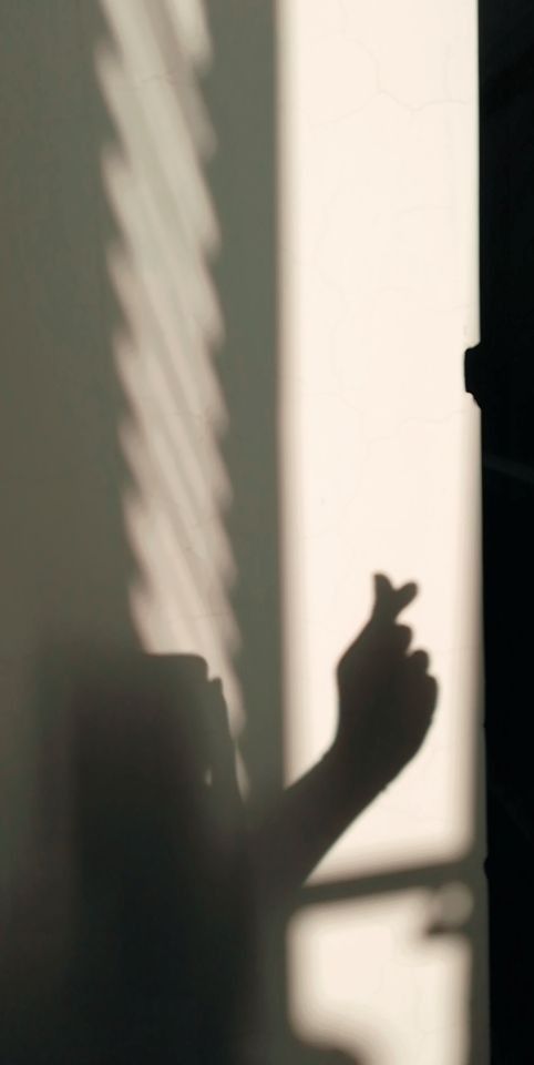 the shadow of a person's hand is cast on a wall by a window