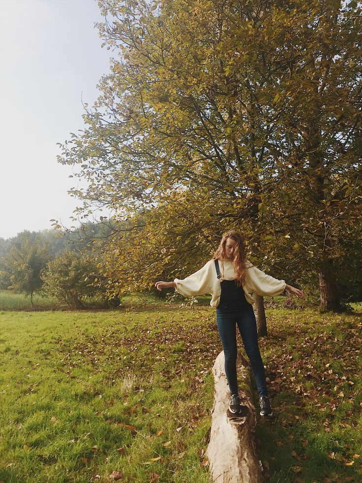 a woman standing on top of a tree stump in the middle of a field with her arms outstretched