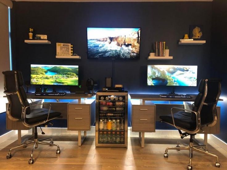 two computer desks with monitors on them in front of a shelf filled with bottles