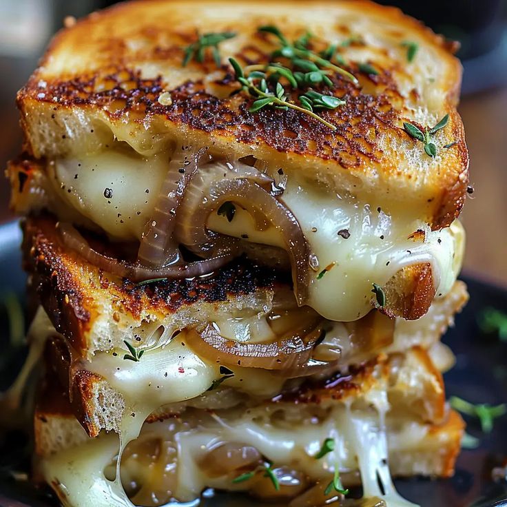 a grilled cheese and onion sandwich on a black plate with green sprigs