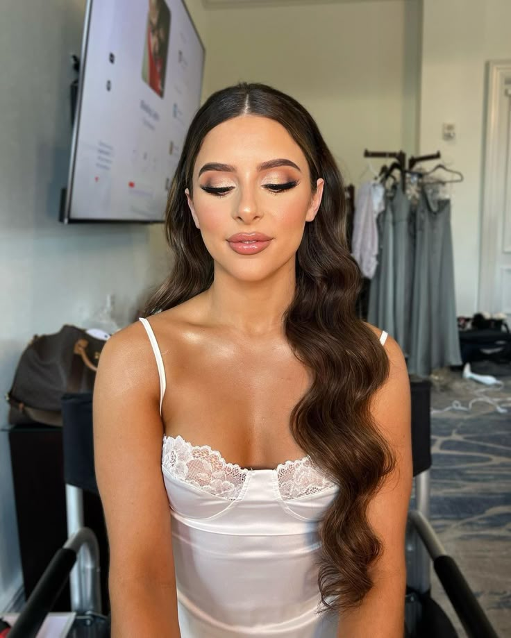 a woman with long brown hair wearing a white dress sitting in front of a mirror