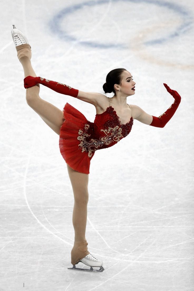 a female figure skating on the ice in a red dress with her arms stretched out