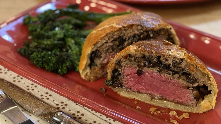 a meatloaf roll on a red plate next to broccoli and bread