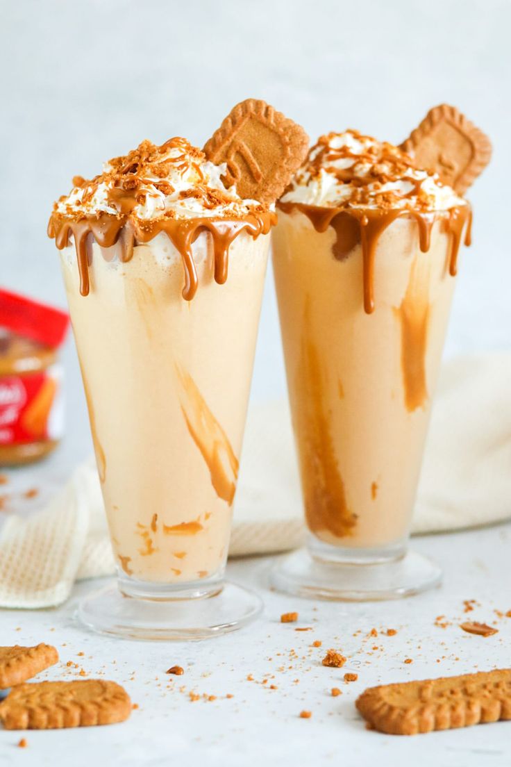 two glasses filled with ice cream and cookies on top of a white table next to crackers