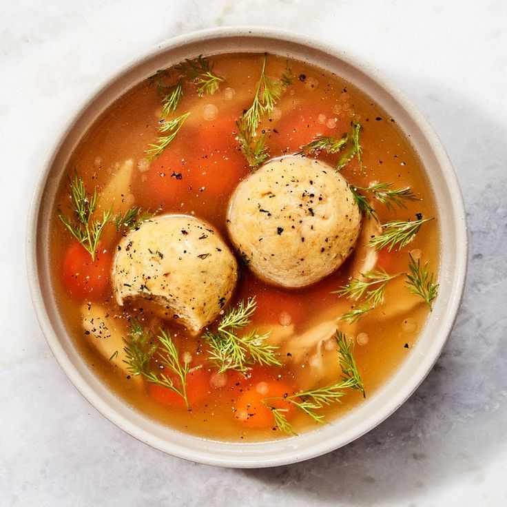 two dumplings sit in a bowl of soup on top of a marble countertop