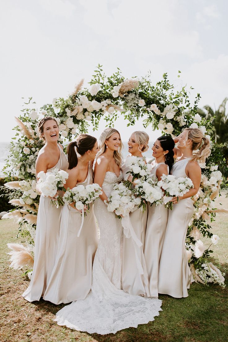 a group of women standing next to each other in front of a flower covered arch