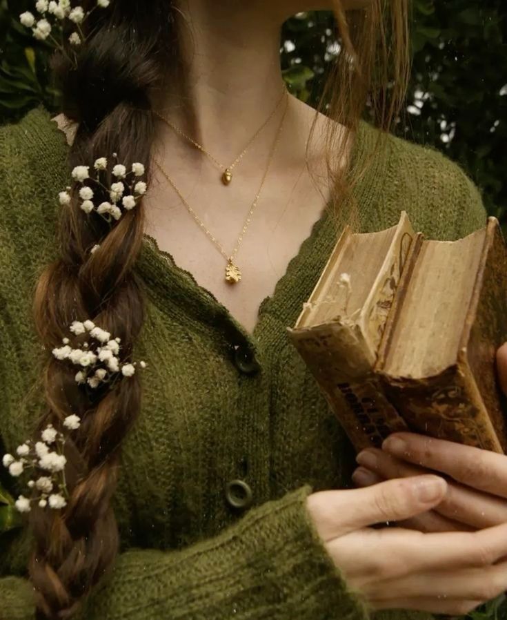 a woman holding an open book with flowers in her hair and wearing a green sweater