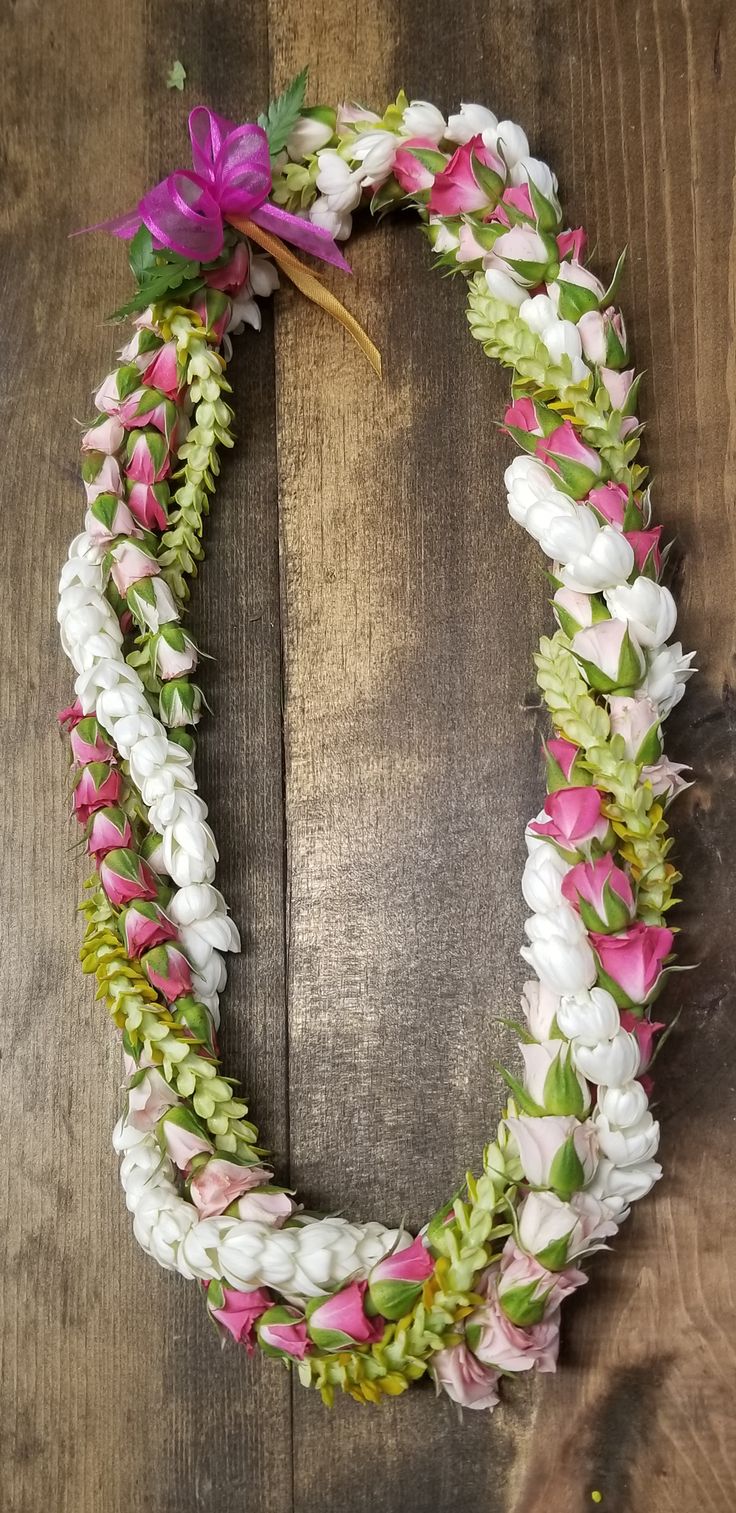 a wreath made out of white and pink flowers on a wooden surface with a purple ribbon