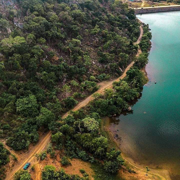 an aerial view of a lake surrounded by green trees and land with cars driving on the road