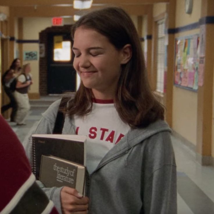 two girls are standing in a hallway and one girl is holding an open book while the other looks at her