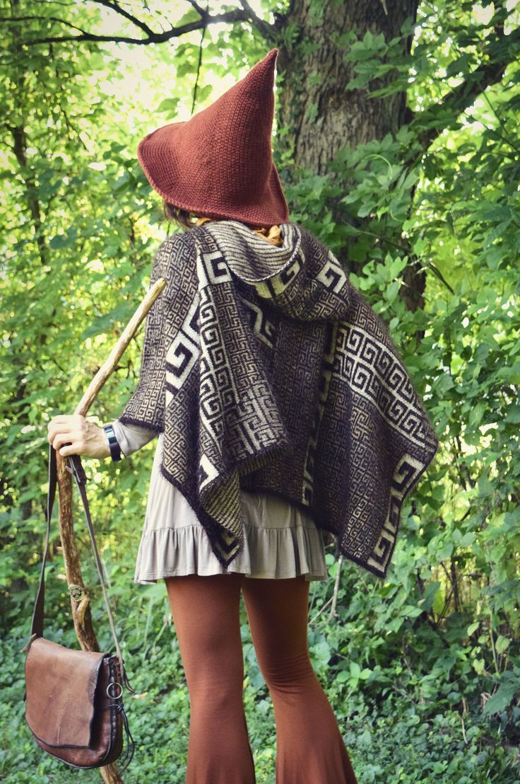 a woman with a brown hat and scarf on walking in the woods holding a purse