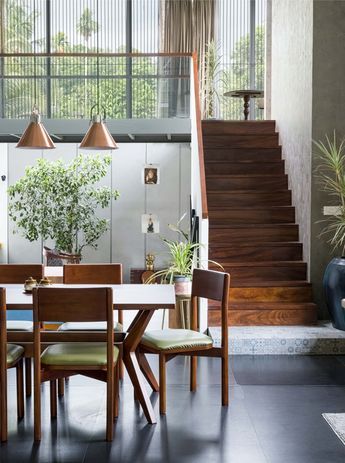 a dining room table and chairs in front of a staircase with potted plants on it