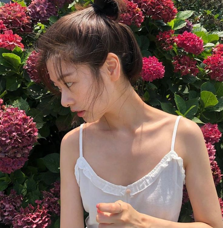 a woman holding a cell phone in front of purple flowers and greenery with her eyes closed