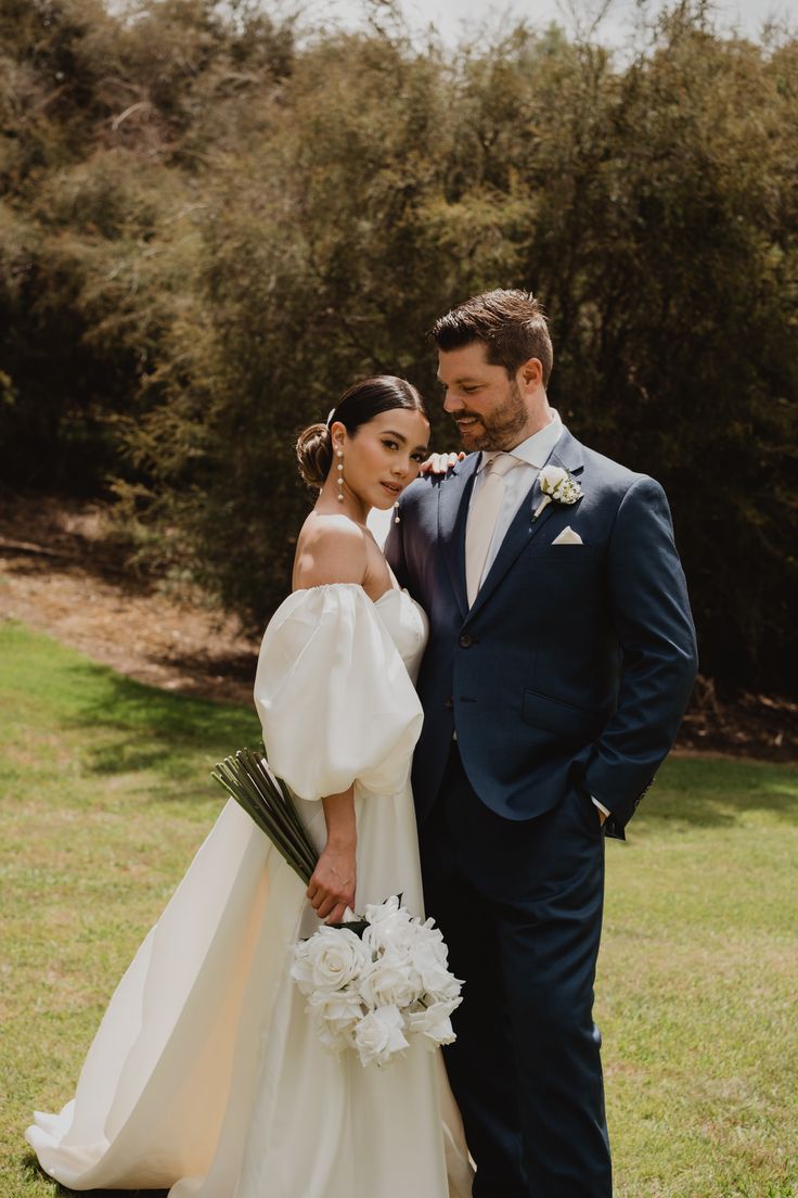 a bride and groom standing in the grass