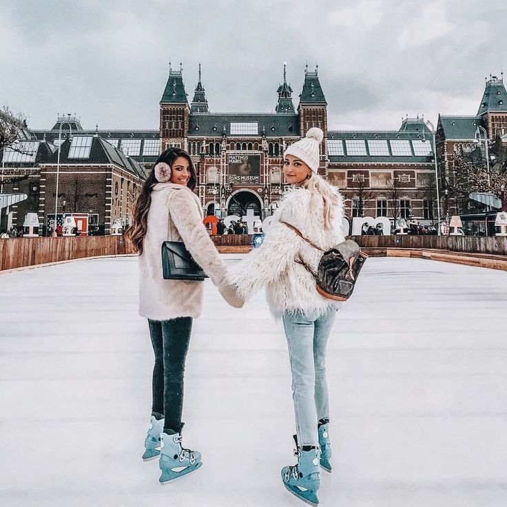 two women standing in front of a large building with snow on the ground and holding hands