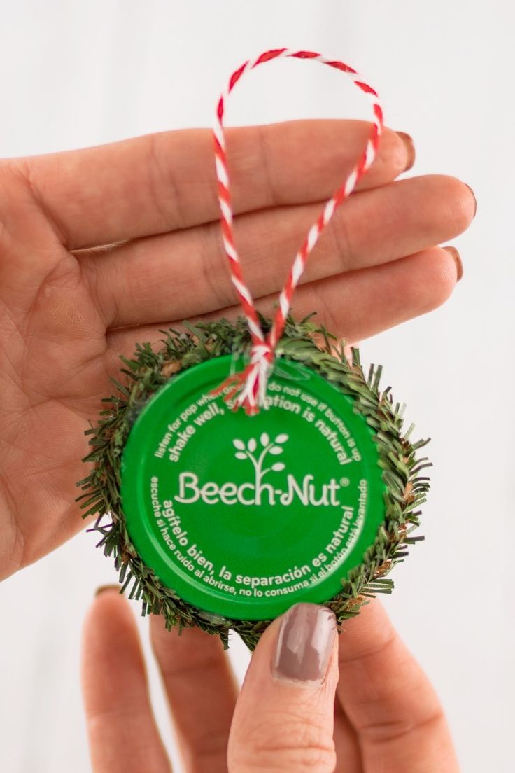 a hand holding a green bottle cap ornament with a red and white string