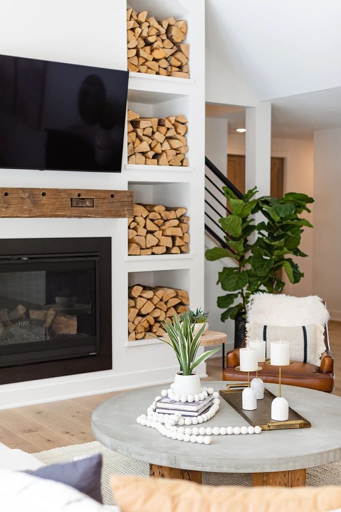 a living room with a fireplace, television and firewood stacked on the wall in front of it