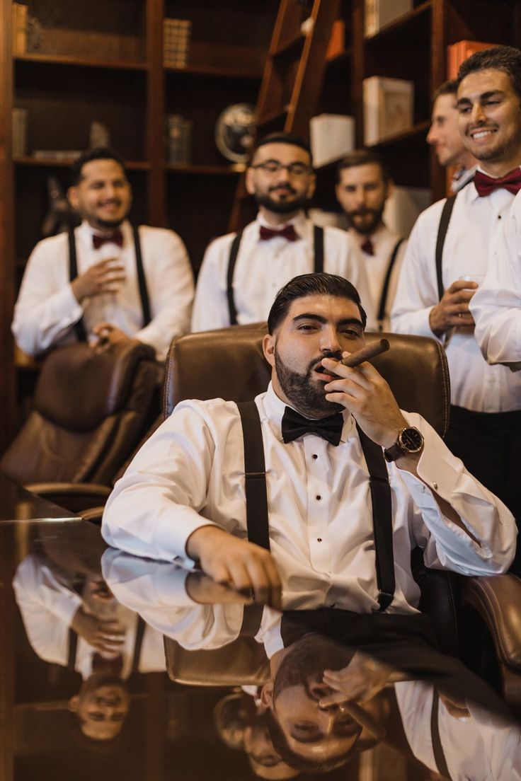 a group of men in white shirts and bow ties sitting at a table with drinks