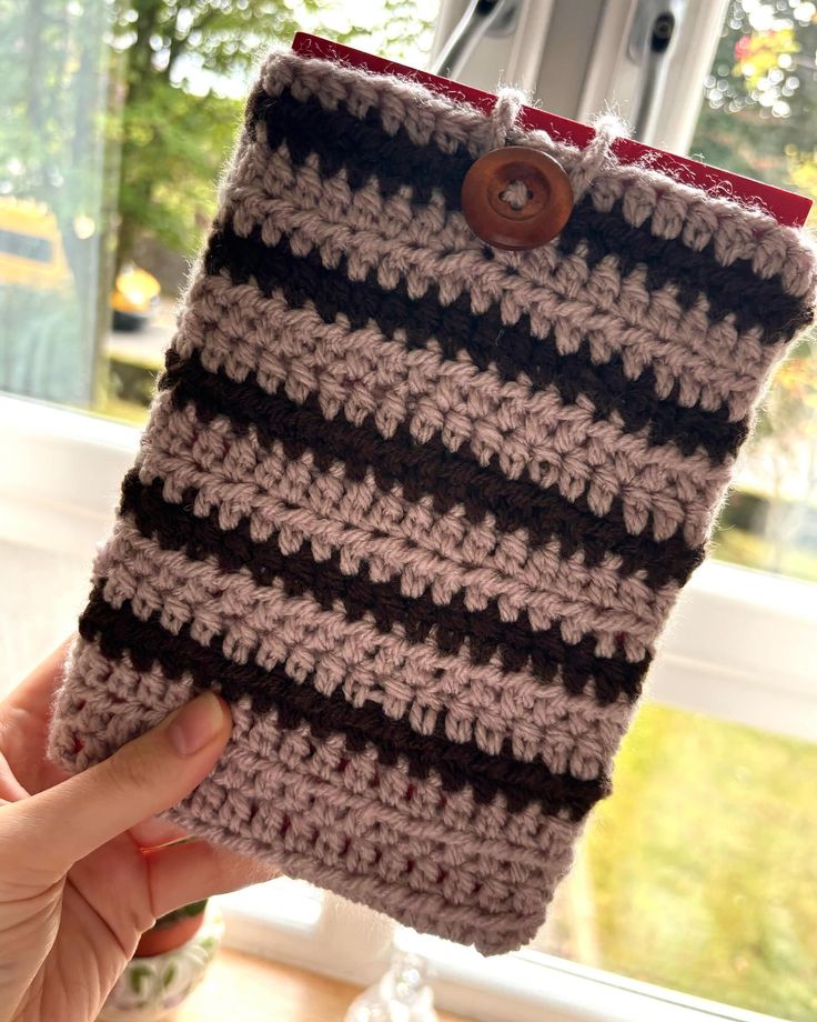 someone is holding up a crocheted case in front of a window with trees outside