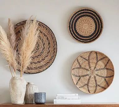 three woven baskets are hanging on the wall above a wooden mantel with two vases