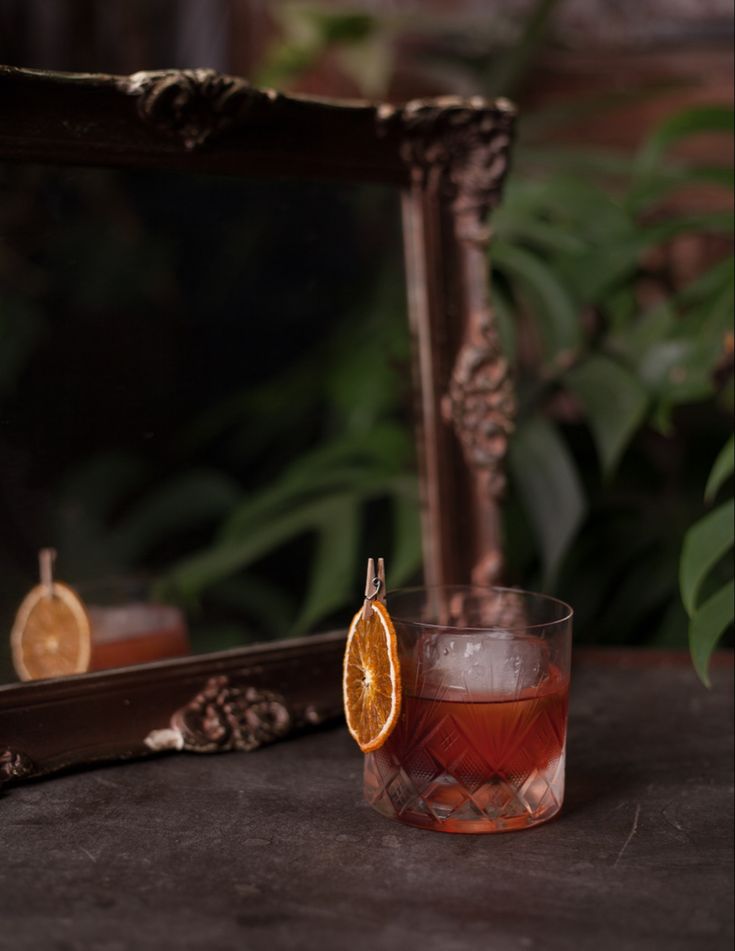 an orange slice sitting on top of a glass filled with liquid next to a mirror