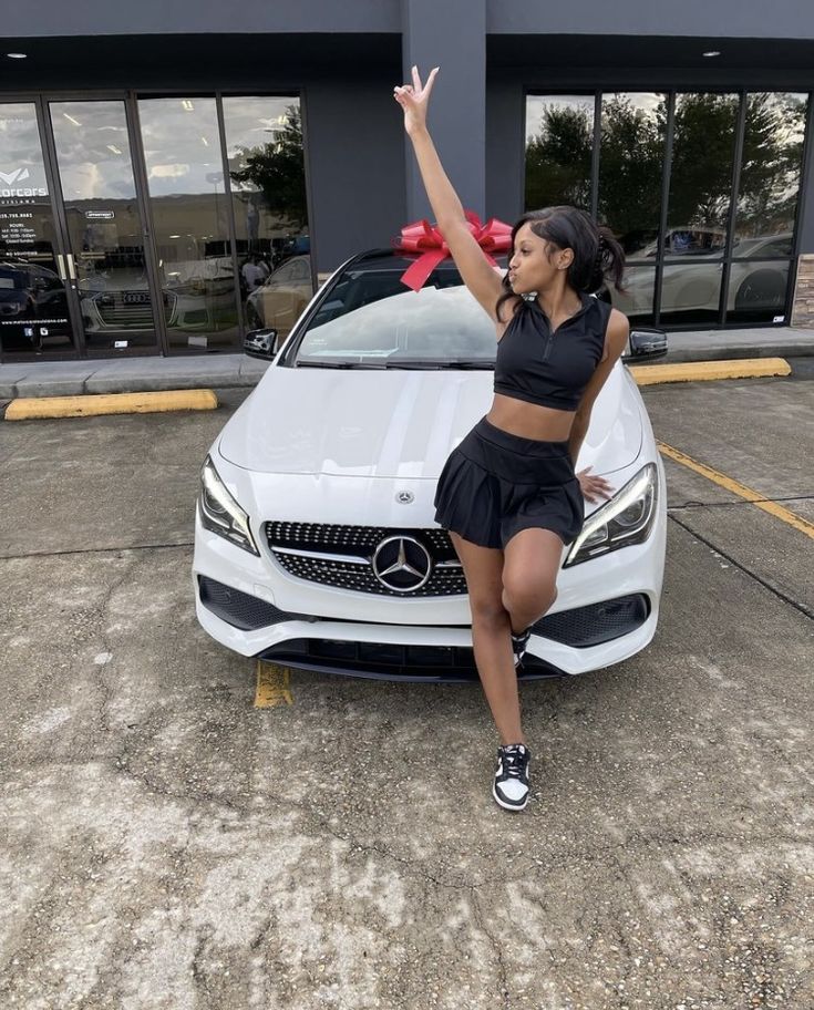 a woman standing next to a white car in front of a building with a red bow on her head