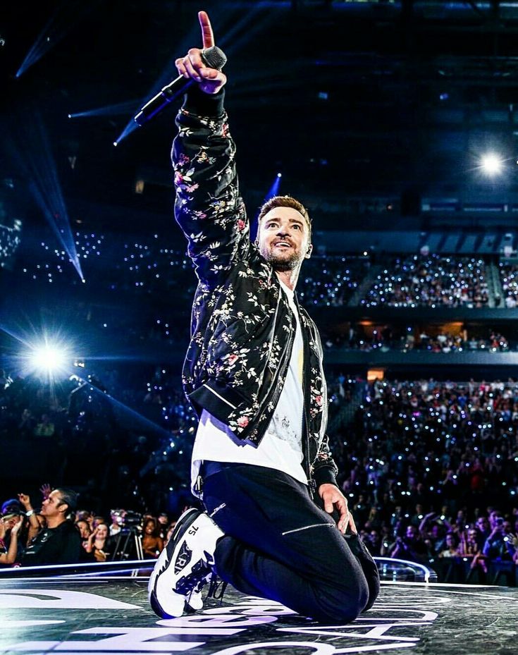 a man sitting on top of a stage with his hand up in the air while holding a microphone