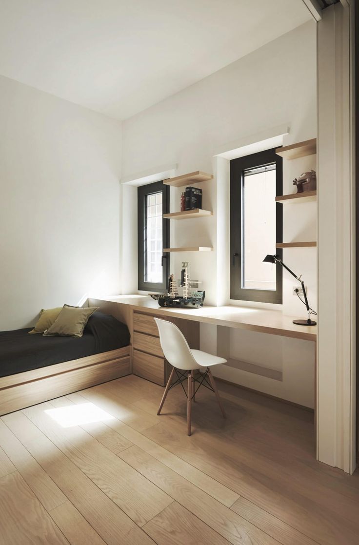 a bedroom with a bed, desk and shelves on the wall next to two windows