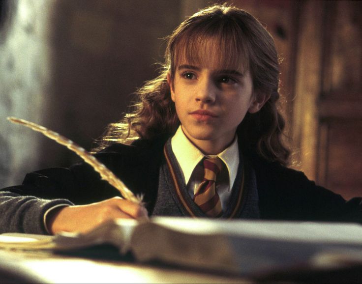 a young person sitting at a desk with a book and pen in their hand, writing