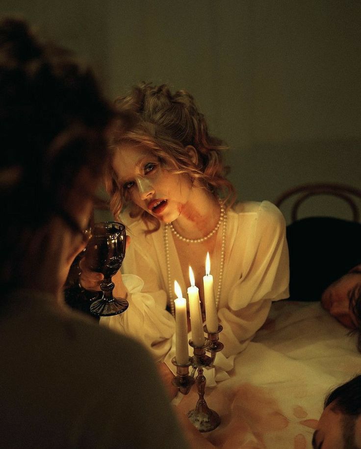 a woman sitting at a table with candles in front of her and other people around her