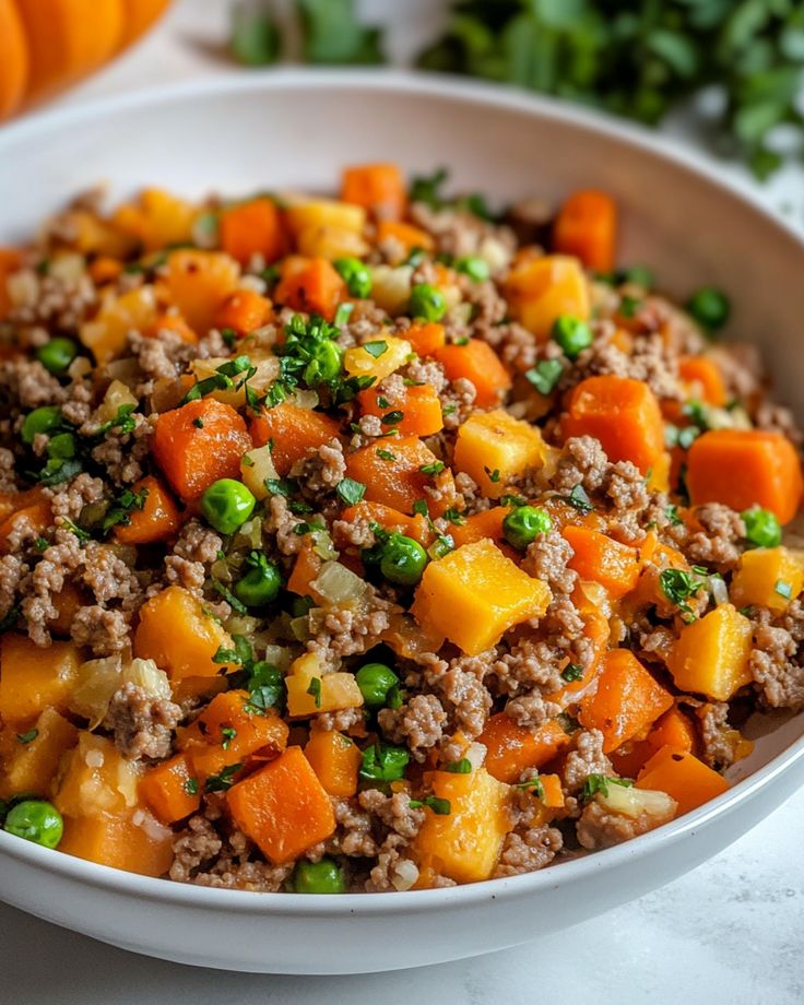 a white bowl filled with meat and veggies on top of a table next to pumpkins