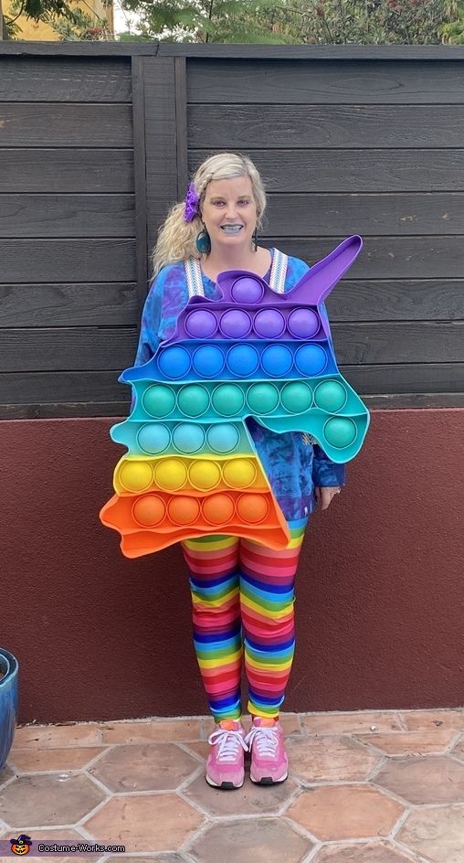 a woman in rainbow colored tights is holding a large plastic toy shaped like a fish