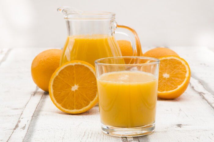 orange juice in a glass and pitcher next to sliced oranges on a white table