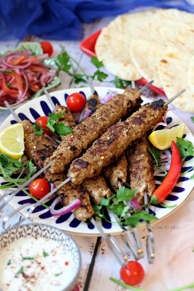 several skewers of meat and vegetables on a plate with pita breads